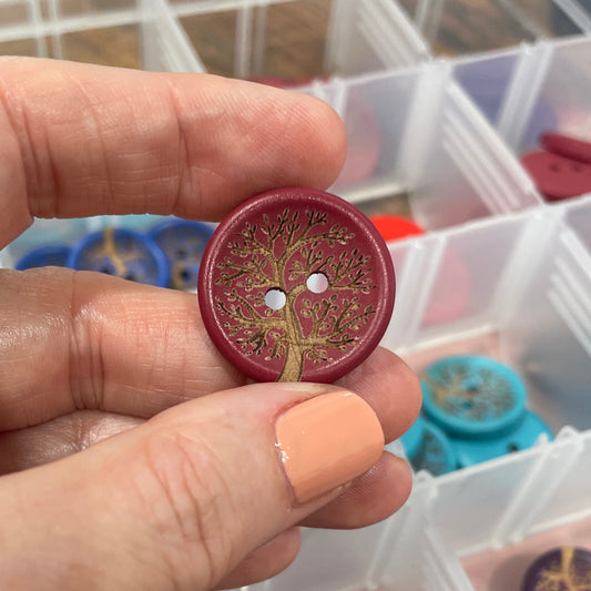 Hand holding a red button with a clear container of buttons in the background