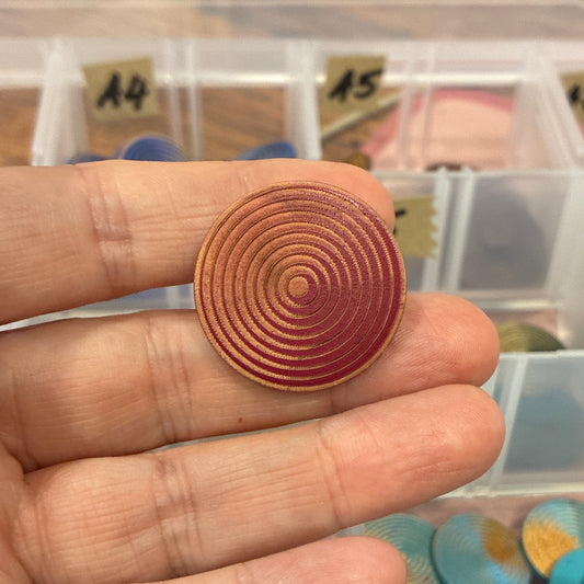 Hand holding a spiral-patterned button with containers of buttons in the background