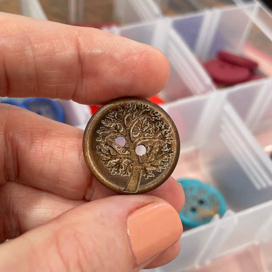 Hand holding a decorative button with a blurred background of button containers.
