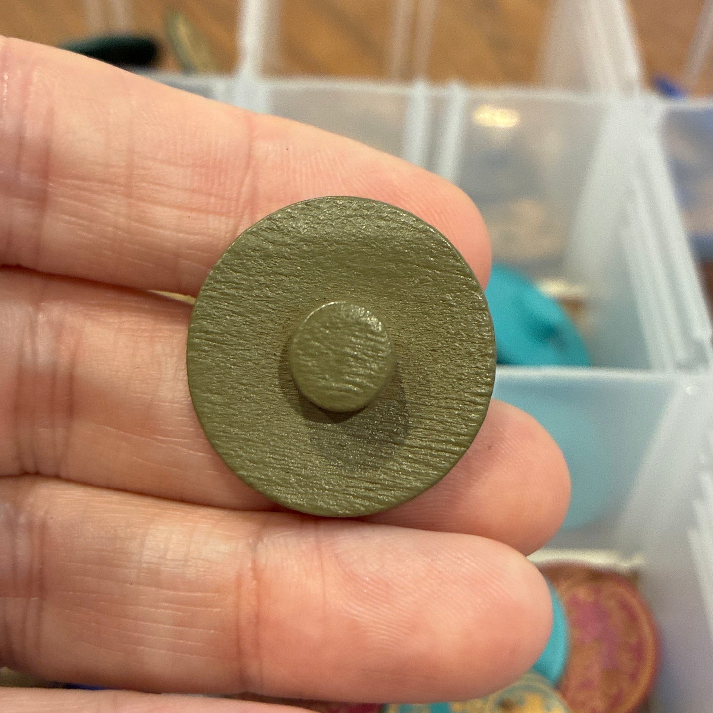 Hand holding a green circular button with a blurred background of colorful items in a box.