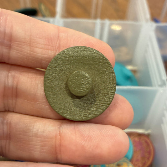 Hand holding a green circular button with a blurred background of colorful items in a box.