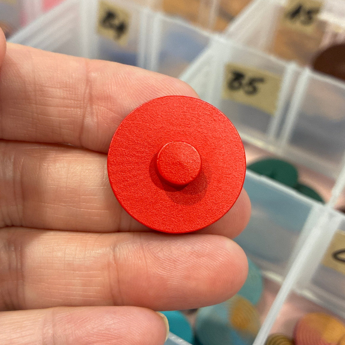 Red button held by a hand with a background of colorful buttons in a case.