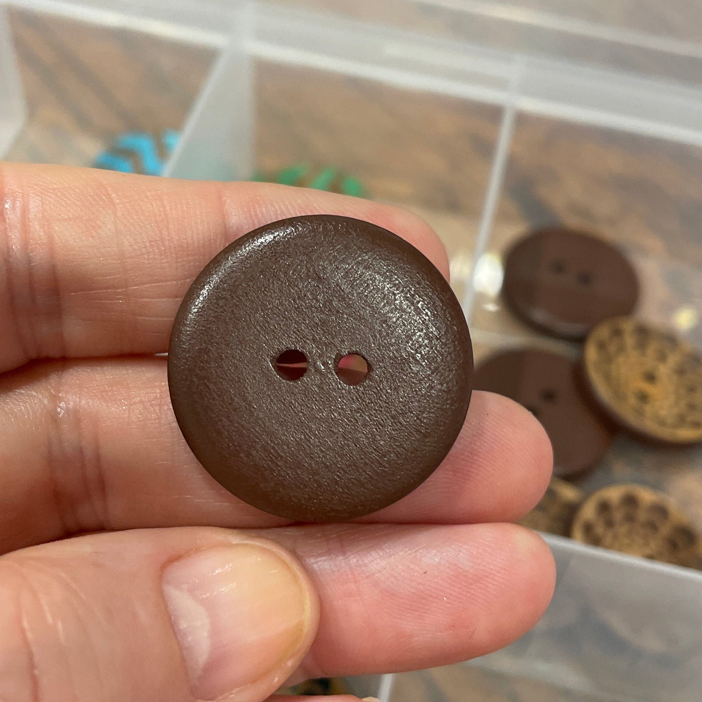 Hand holding a brown button with a blurred background of button collection