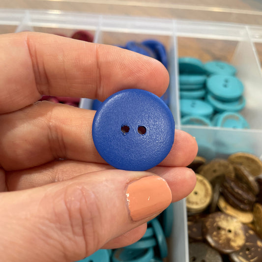 Hand holding a blue button with a container of buttons in the background
