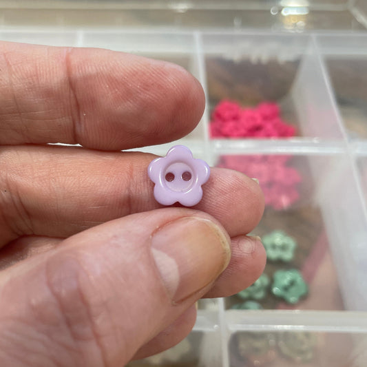 Hand holding a small purple flower-shaped object with a display of similar objects in the background.