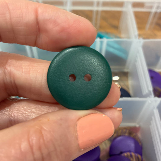 Hand holding a green button with a container of buttons in the background