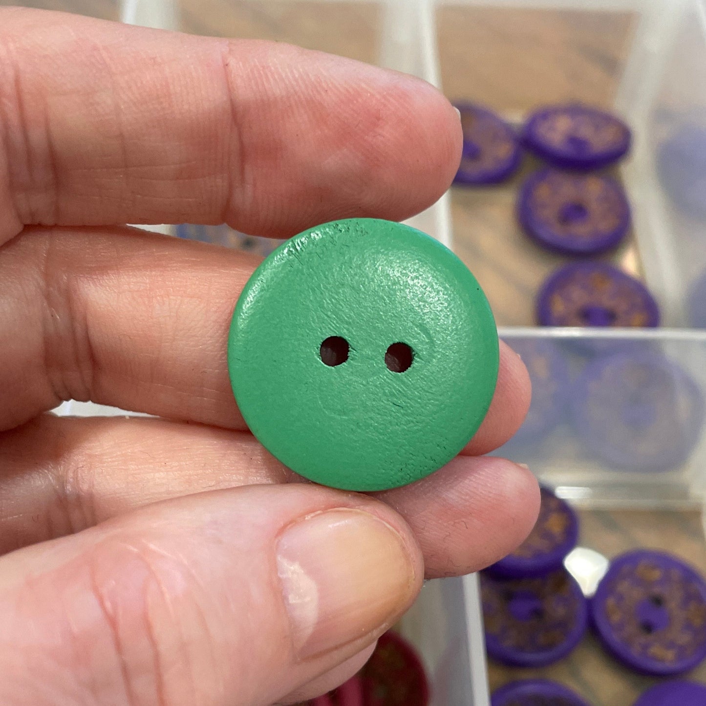 Hand holding a green button with a collection of buttons in a box in the background