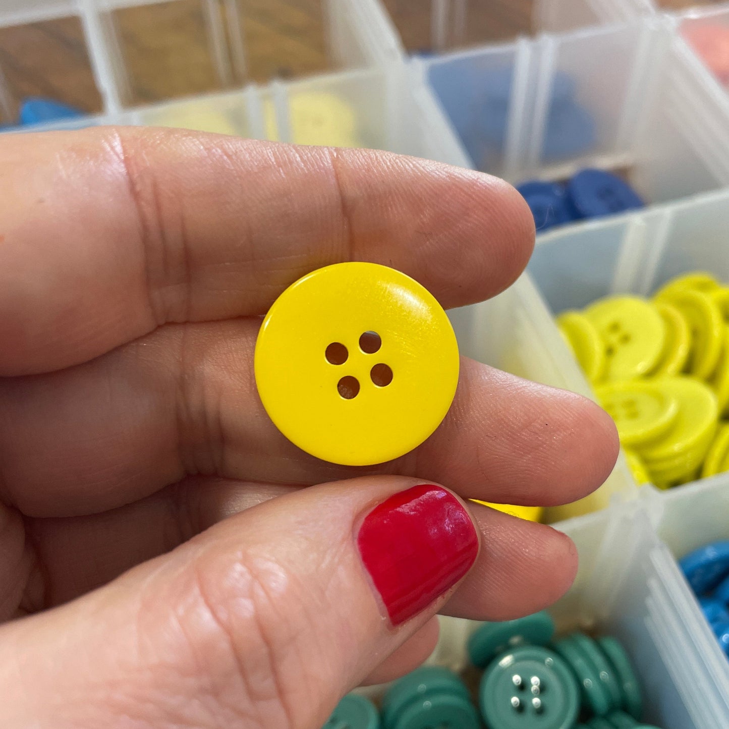 Hand holding a yellow button with a container of colorful buttons in the background