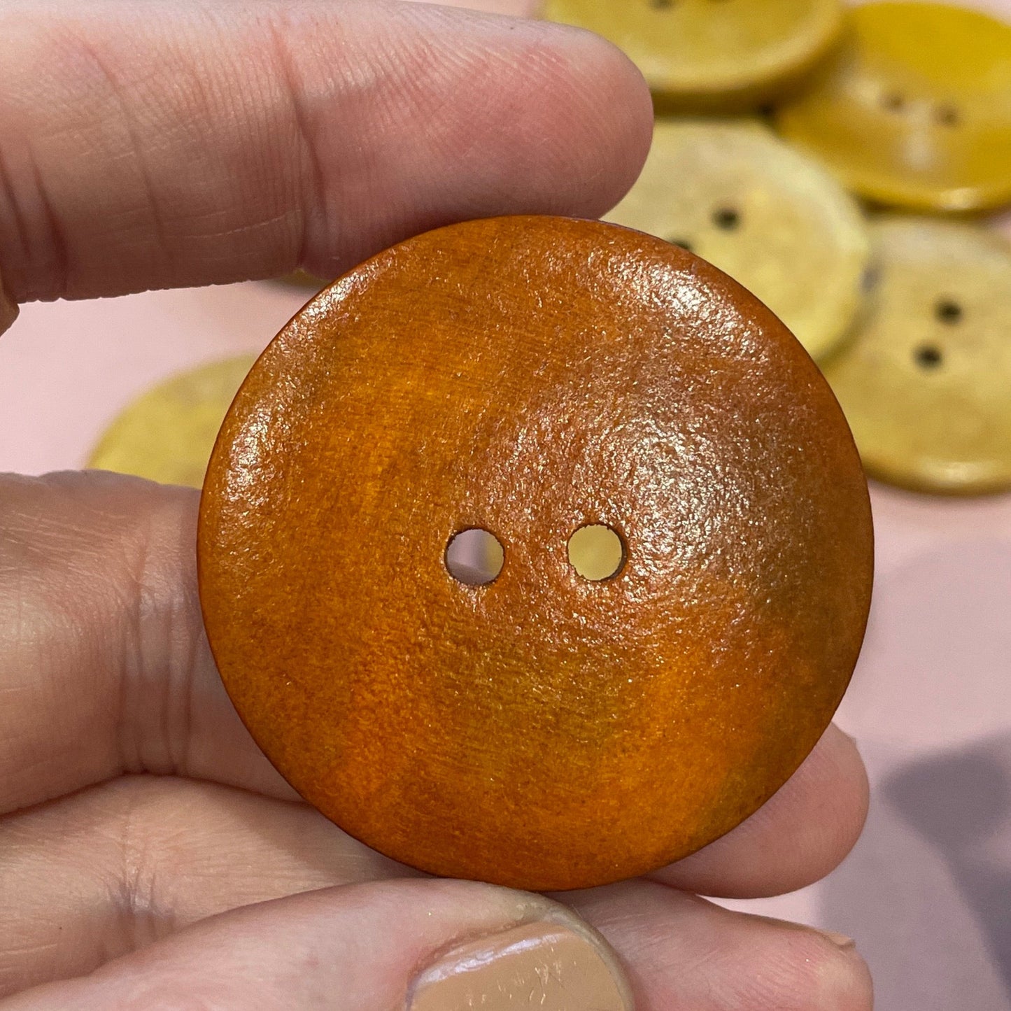 Hand holding a brown button with colorful buttons in the background on a pink surface.