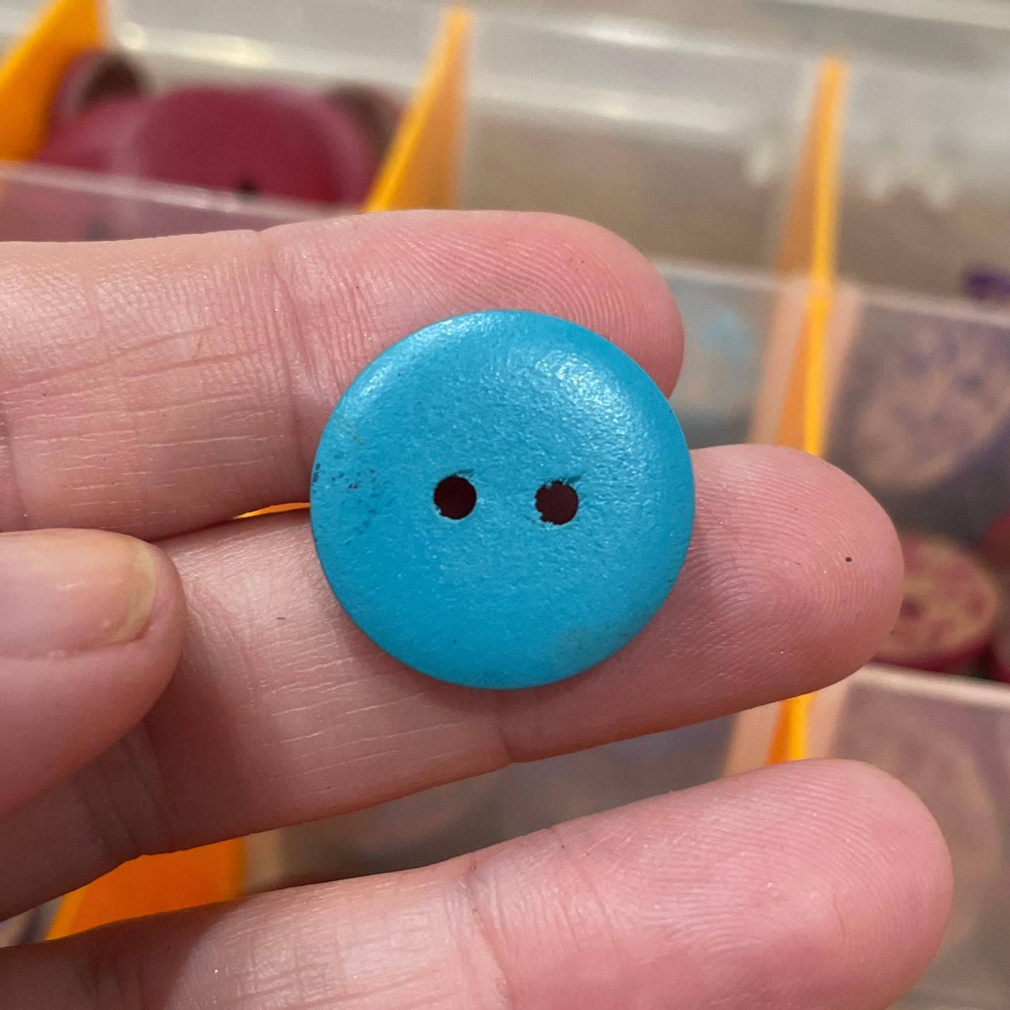 Hand holding a blue button with a blurred background of a button collection.
