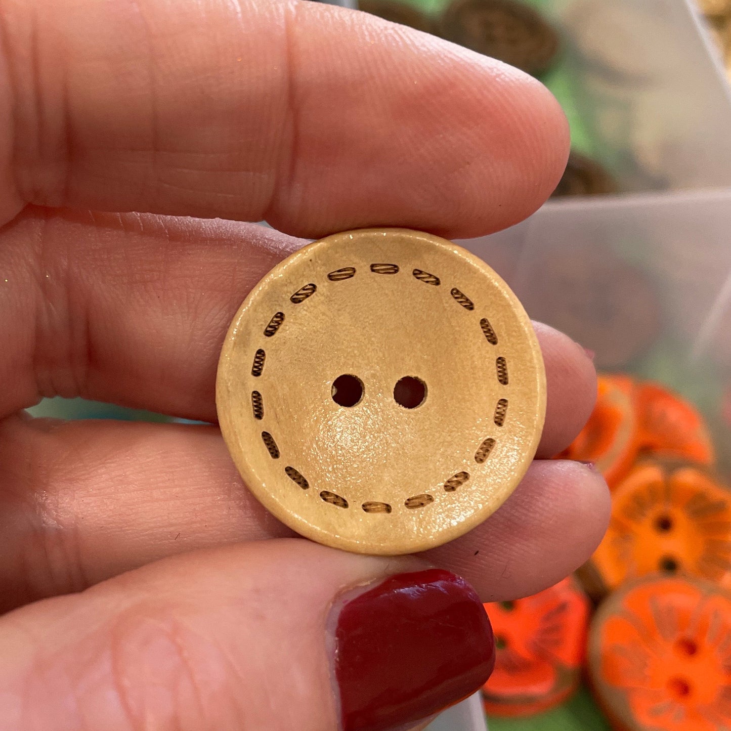 Hand holding a wooden button with a background of colorful buttons
