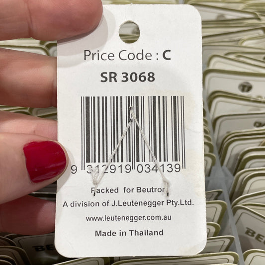 Hand holding a tag with a barcode and product details, surrounded by similar tags.