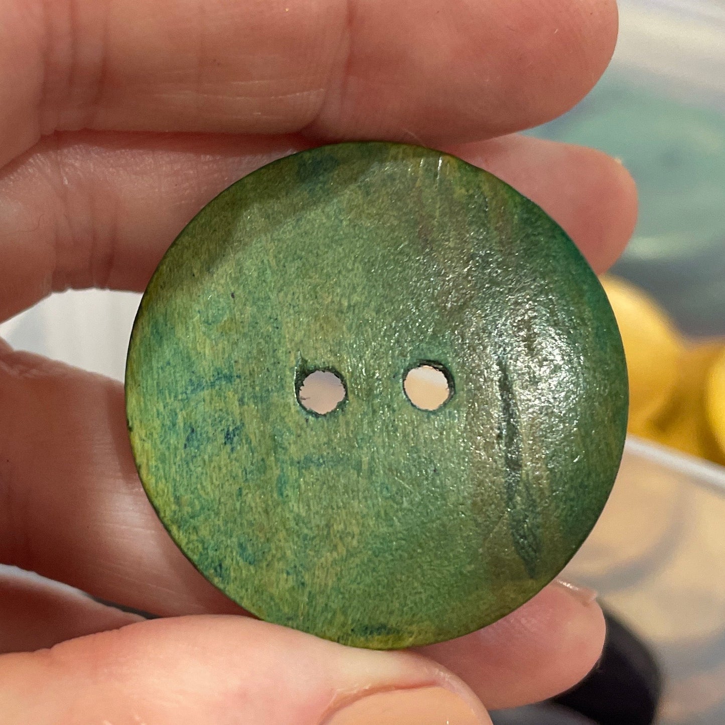 Green button held in a hand with a blurred background of buttons