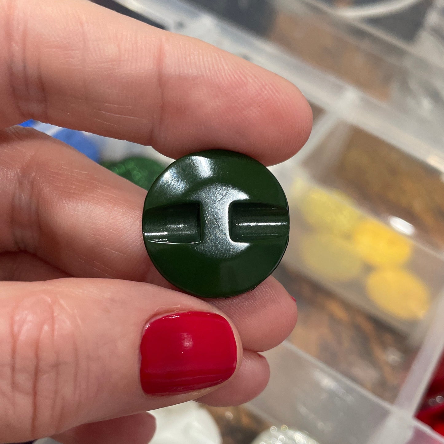 Hand holding a green button with a blurred background of a button collection.
