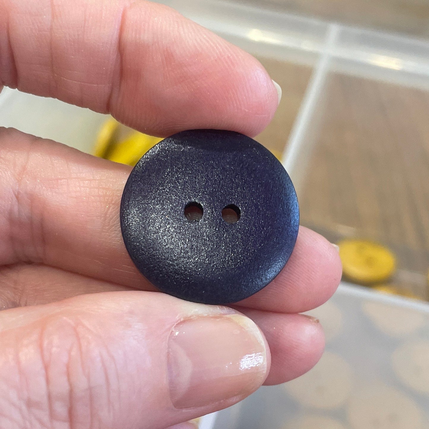 Hand holding a purple button with a container of buttons in the background