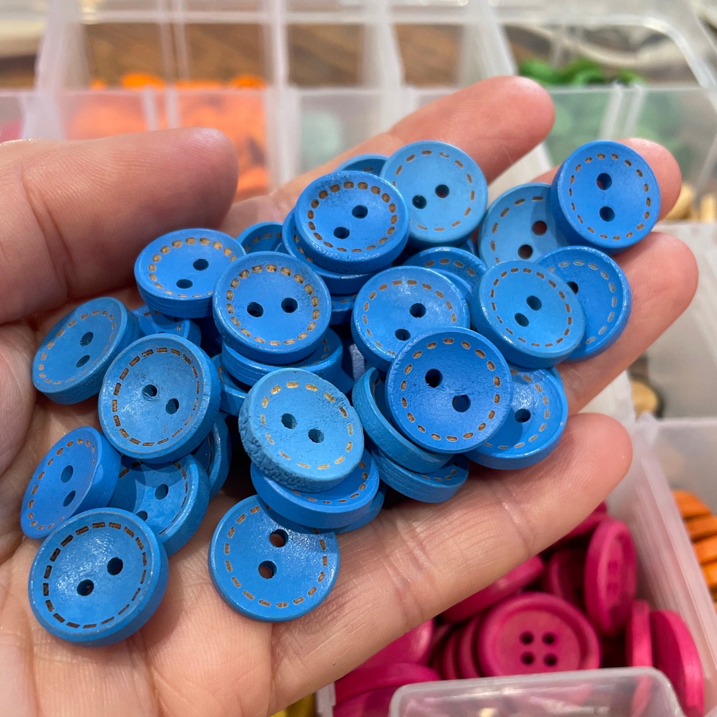 Hand holding blue buttons with a container of assorted buttons in the background