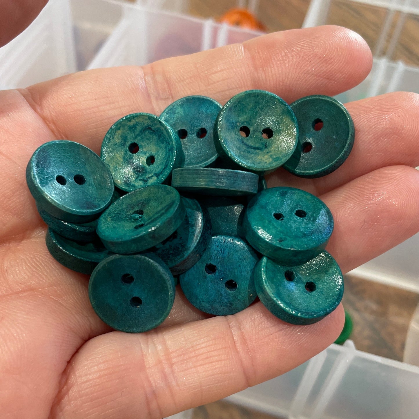 Hand holding green buttons with a container of buttons in the background