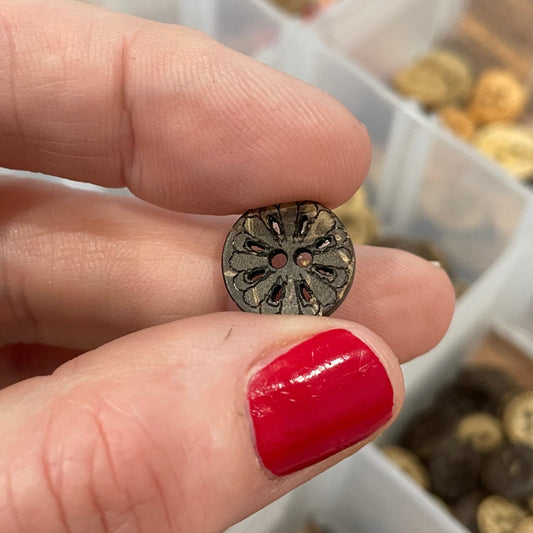 Hand holding a decorative button with a background of button assortment in a box.