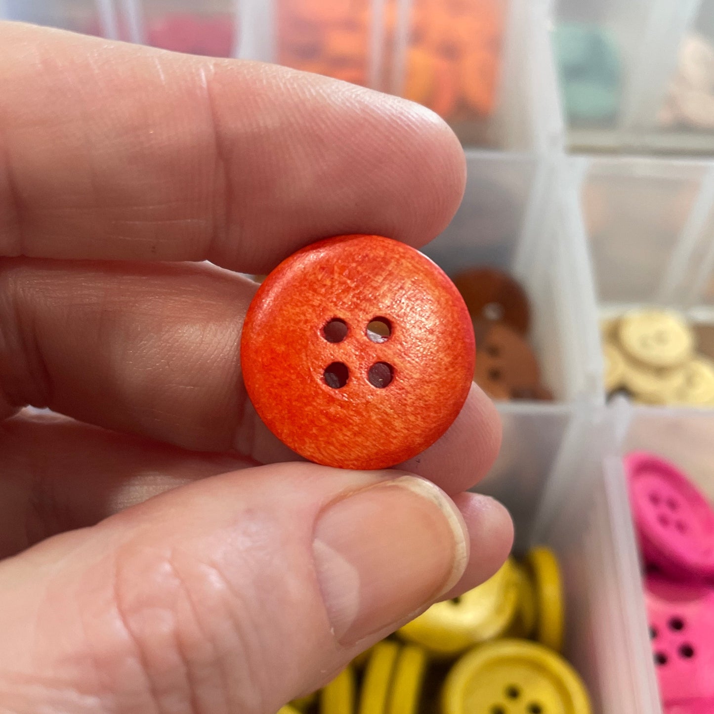 Hand holding an orange button with a container of buttons in the background