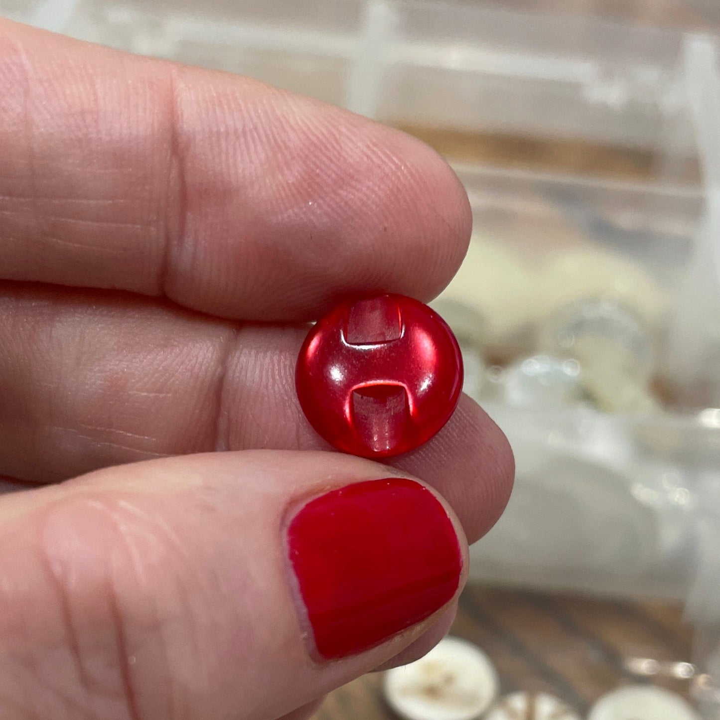 Red buttons held between fingers with a container of buttons in the background