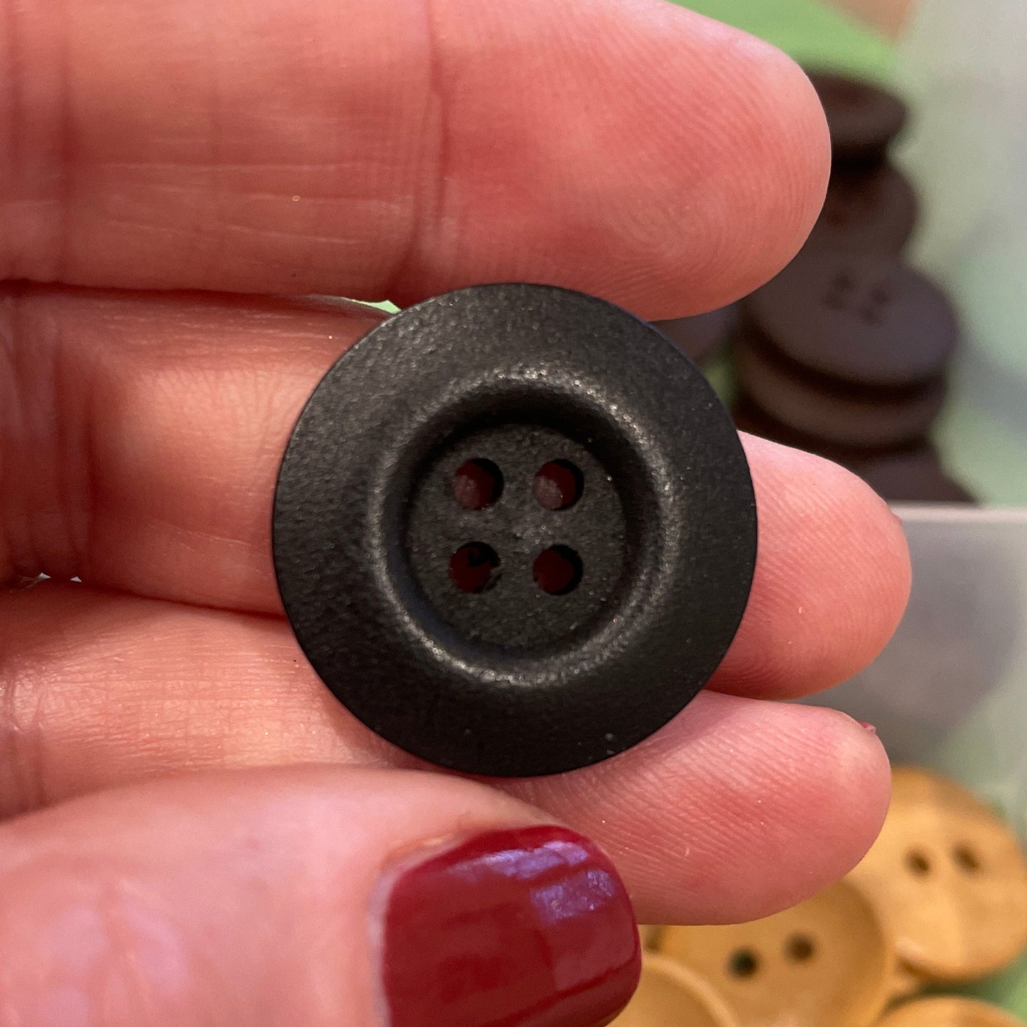 Hand holding a black button with a container of gold buttons in the background