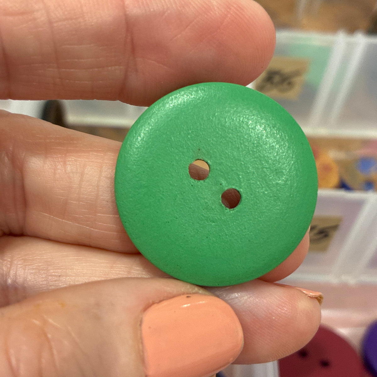 Green button held between fingers with a container of buttons in the background