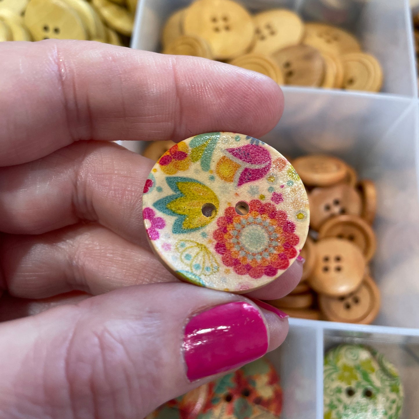 Hand holding a decorative button with a colorful design, surrounded by various buttons in the background.