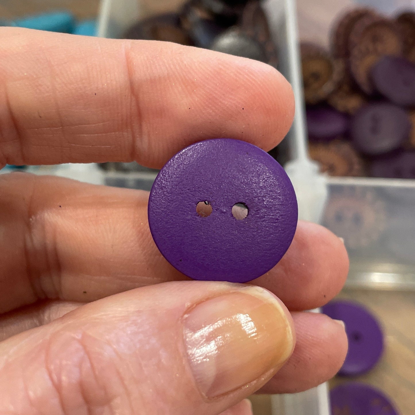 Hand holding a purple button with a blurred background of button collection