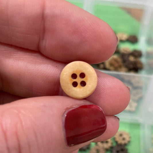 Hand holding a small yellow button with a clear container of buttons in the background