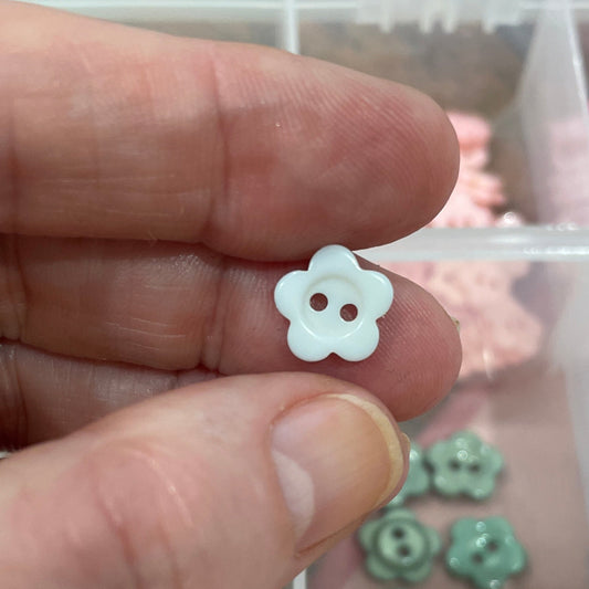 Hand holding a small white flower-shaped object with a clear container of assorted colorful flowers in the background.