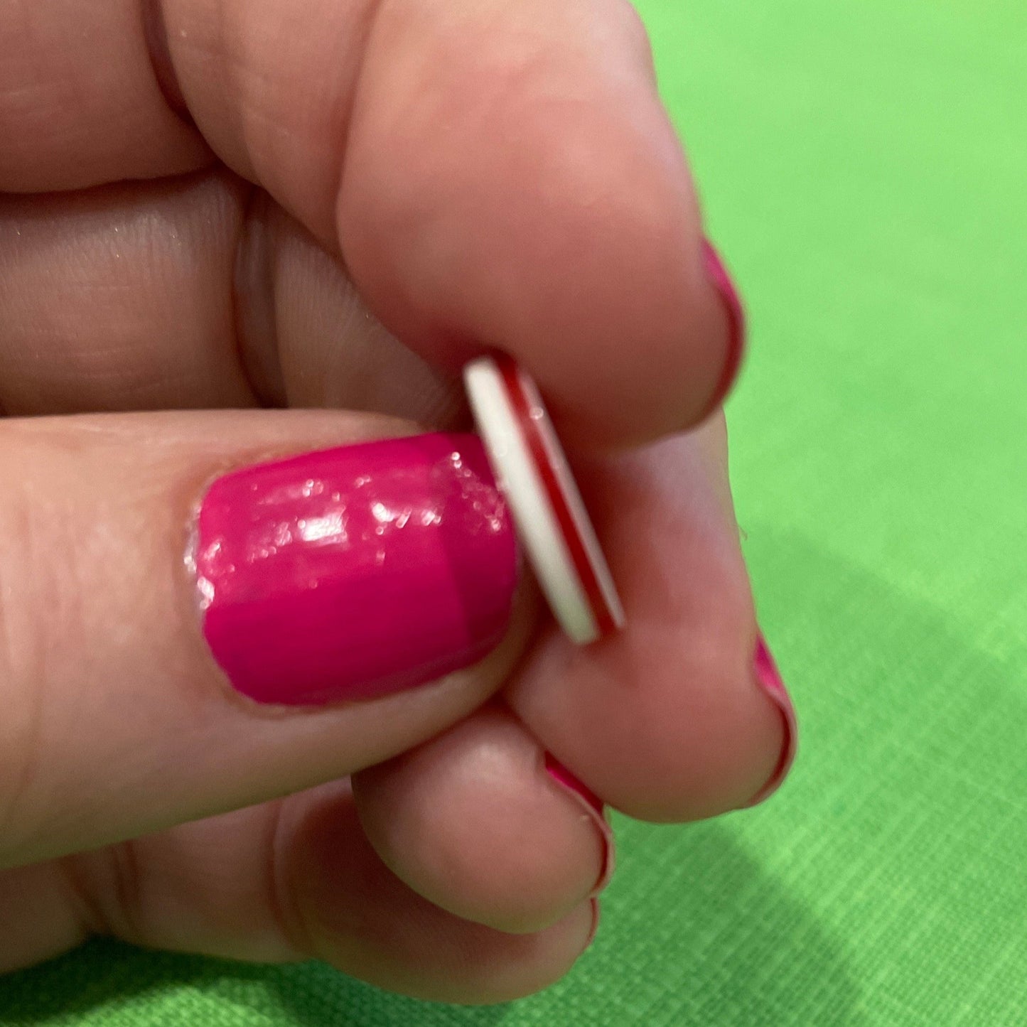 Hand holding a small cylindrical object with pink nail polish against a green background