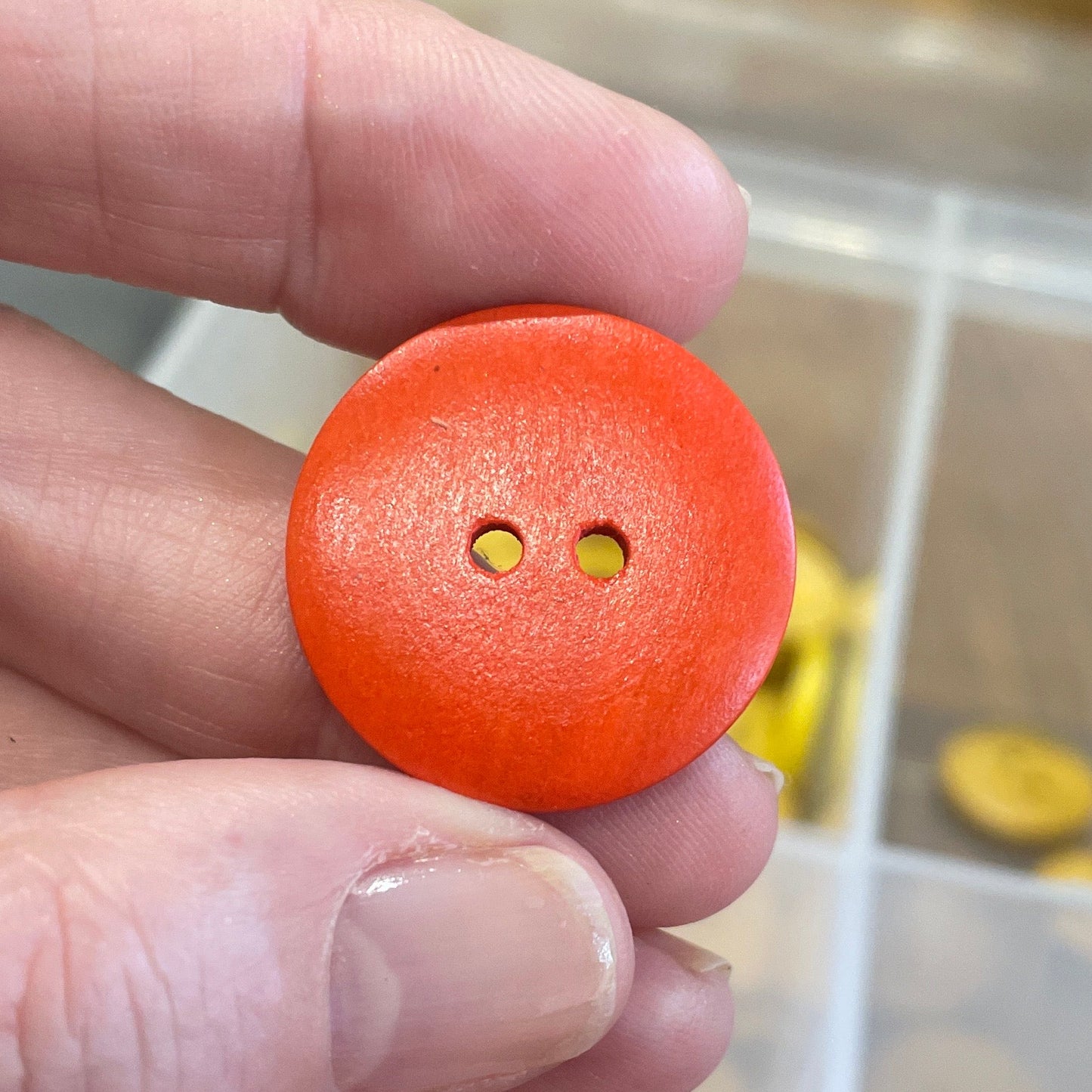 Hand holding an orange button with a container of buttons in the background