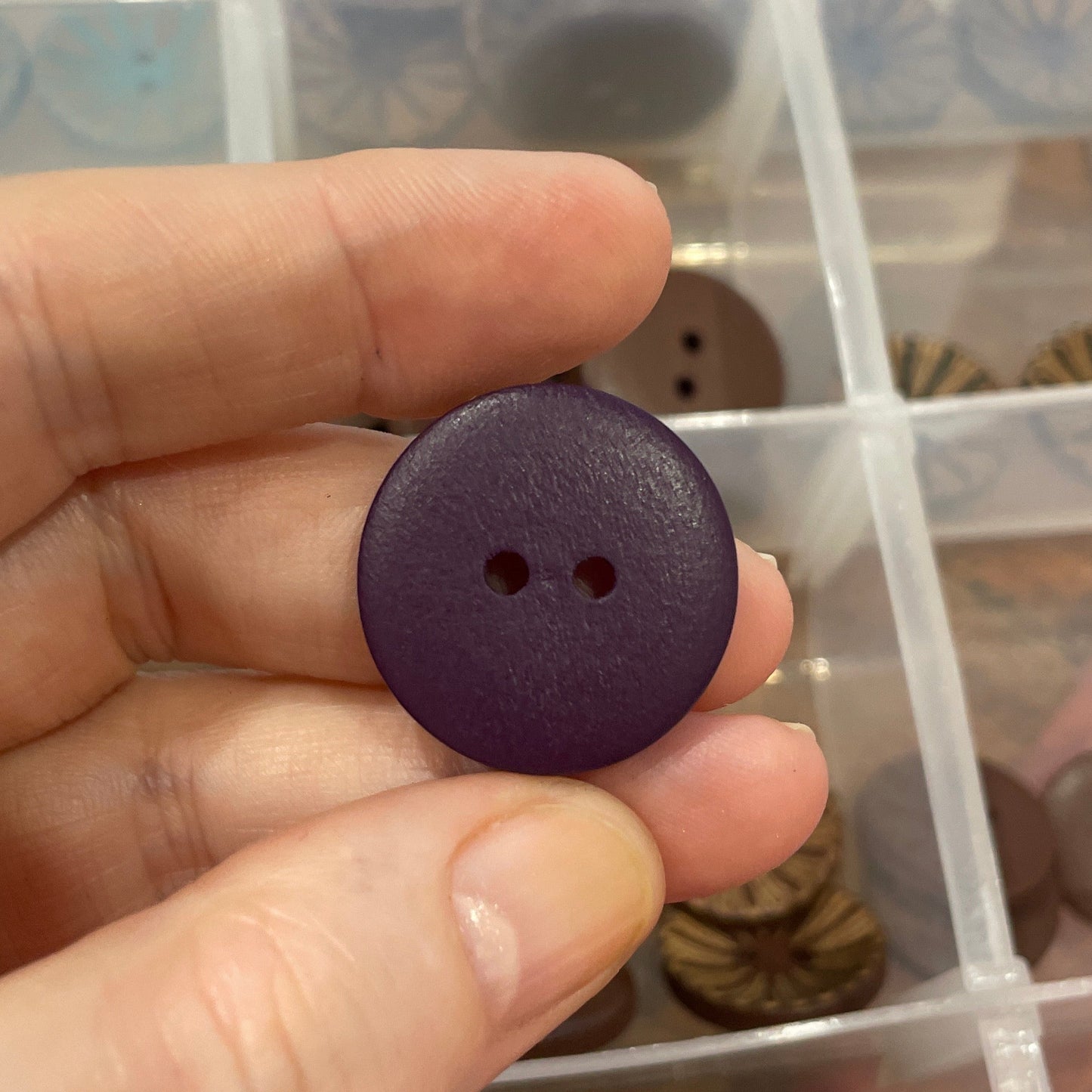 Hand holding a purple button with a clear container of assorted buttons in the background