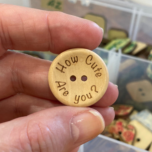 Hand holding a gold button with text, with a container of various buttons in the background