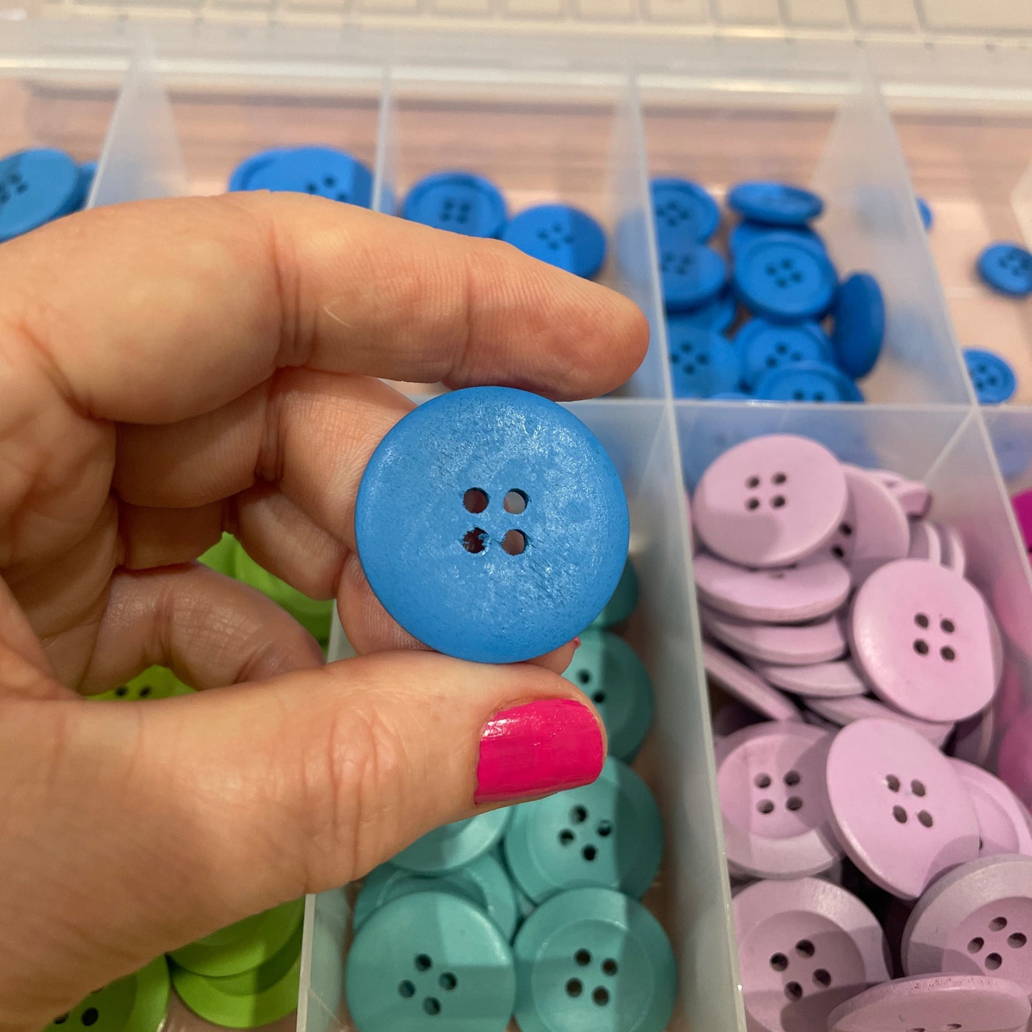 Hand holding a blue button with a container of colorful buttons in the background