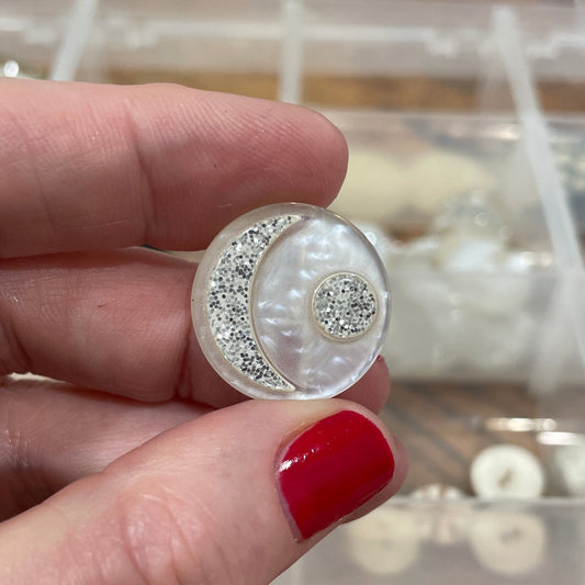 Hand holding a decorative button with a blurred background of a button organizer.