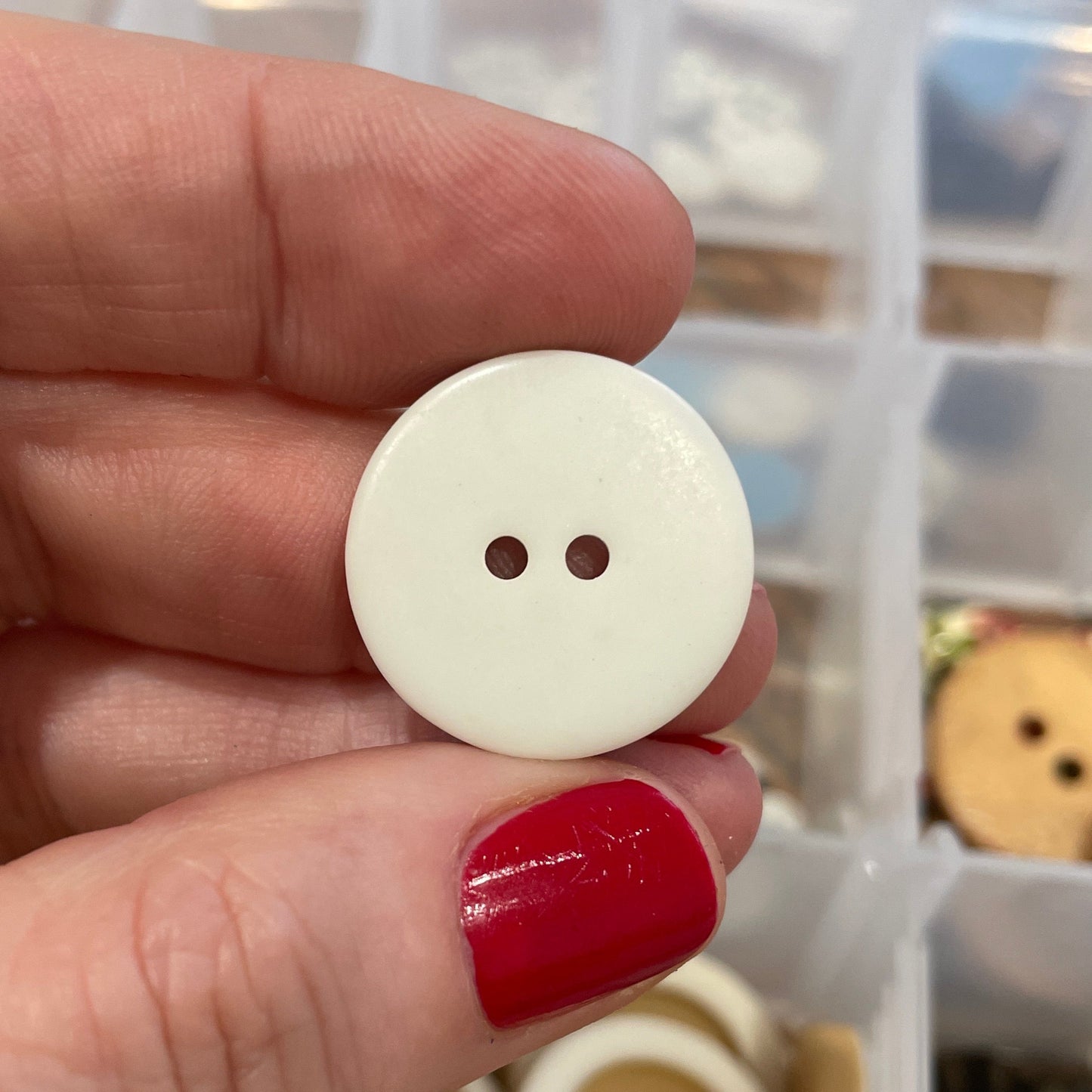 Hand holding a white button with a clear container of buttons in the background