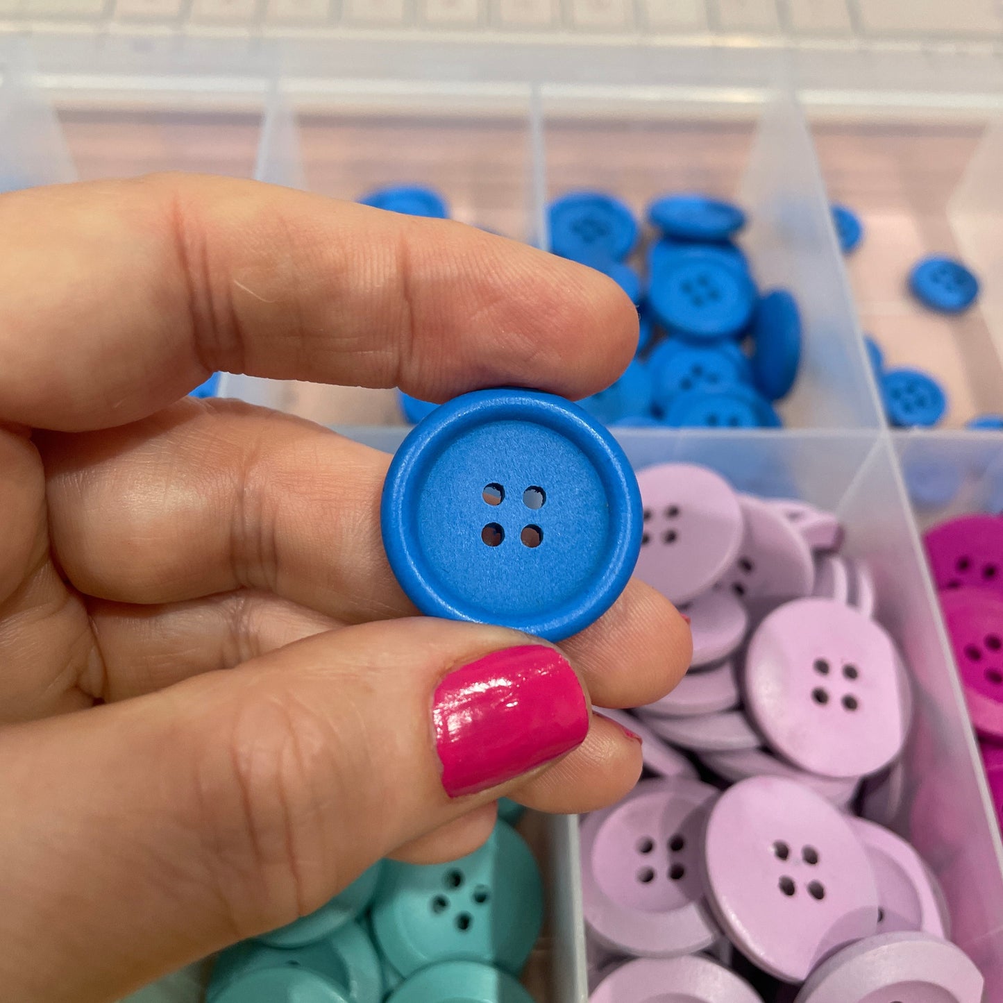 Hand holding a blue button with a container of colorful buttons in the background