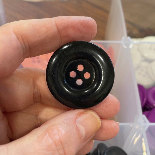 Hand holding a black button with a clear container of buttons in the background