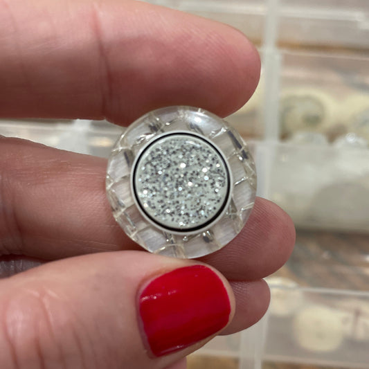 Close-up of a hand holding a decorative button with a blurred background of buttons.