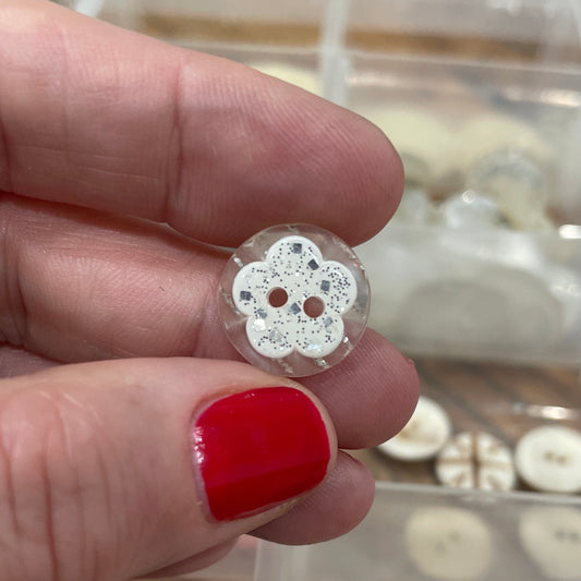 Close-up of a hand holding a silver earring with a red nail polish against a blurred background of buttons.