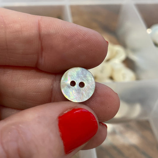 Hand holding a small button with a blurred container of buttons in the background