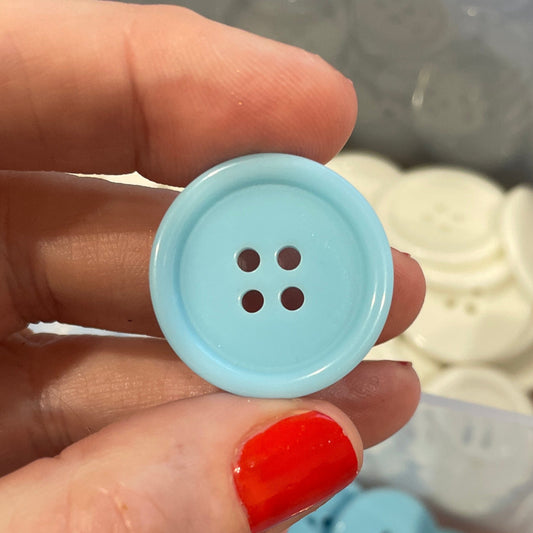 Hand holding a blue button with a container of buttons in the background