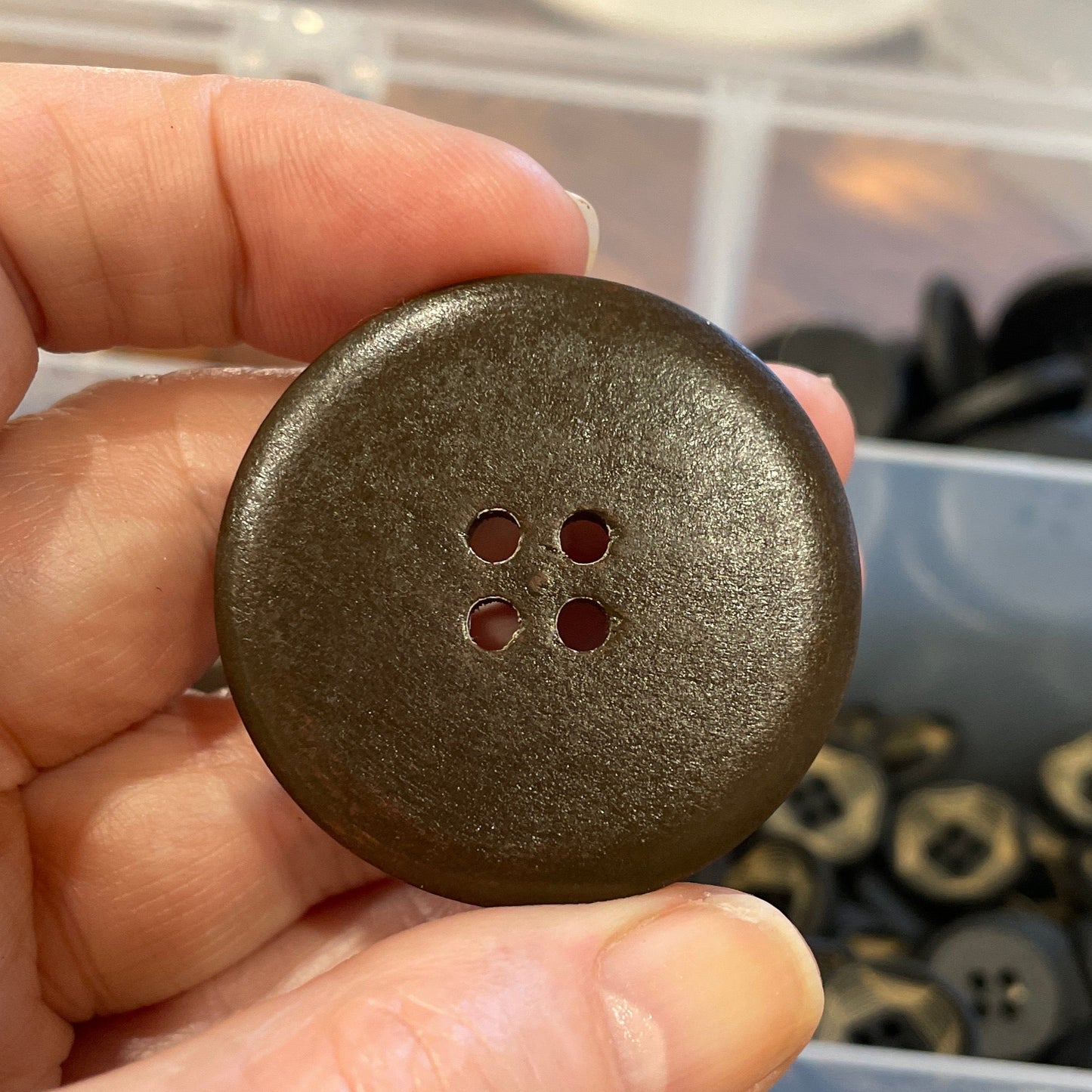 Hand holding a dark brown button with a blurred background of buttons