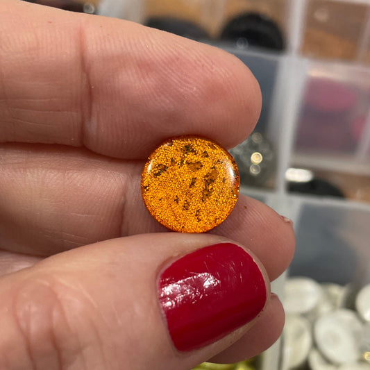 Hand holding a small orange object with a blurred container of colorful objects in the background