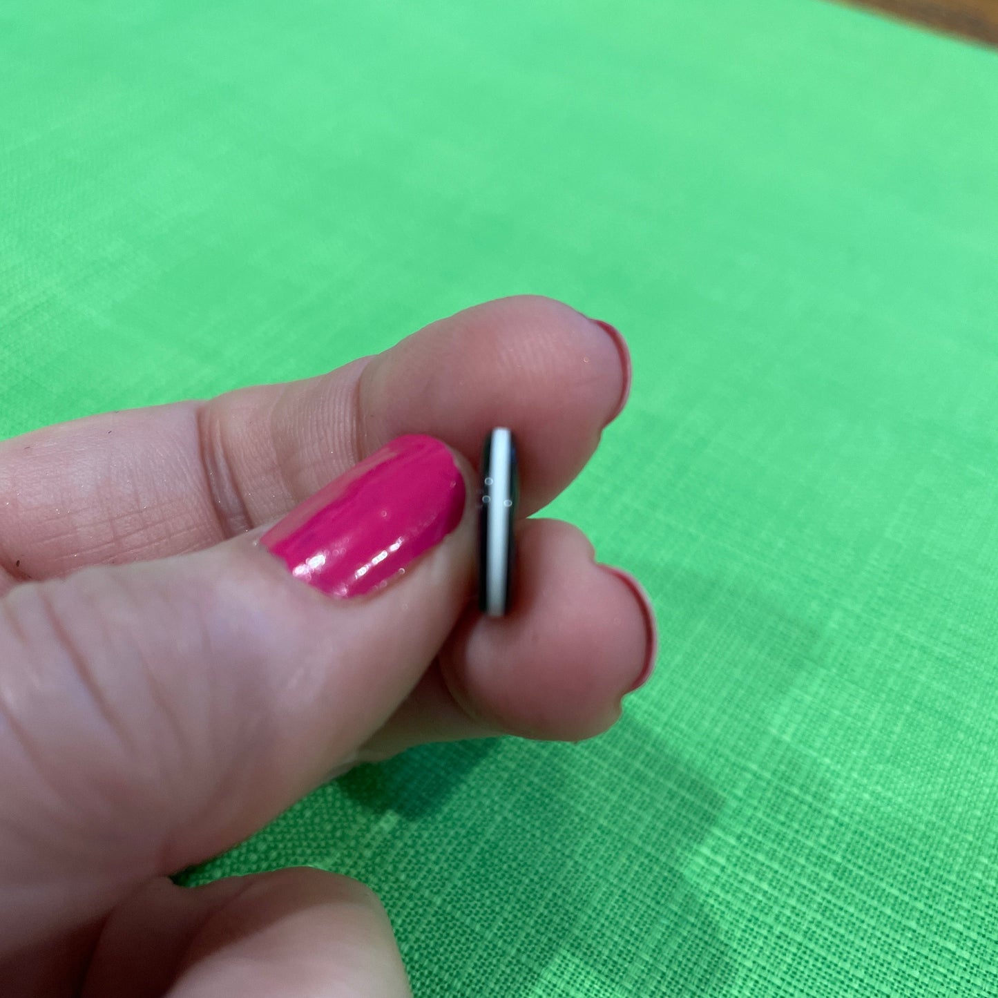 Hand holding a small metallic object against a green fabric background