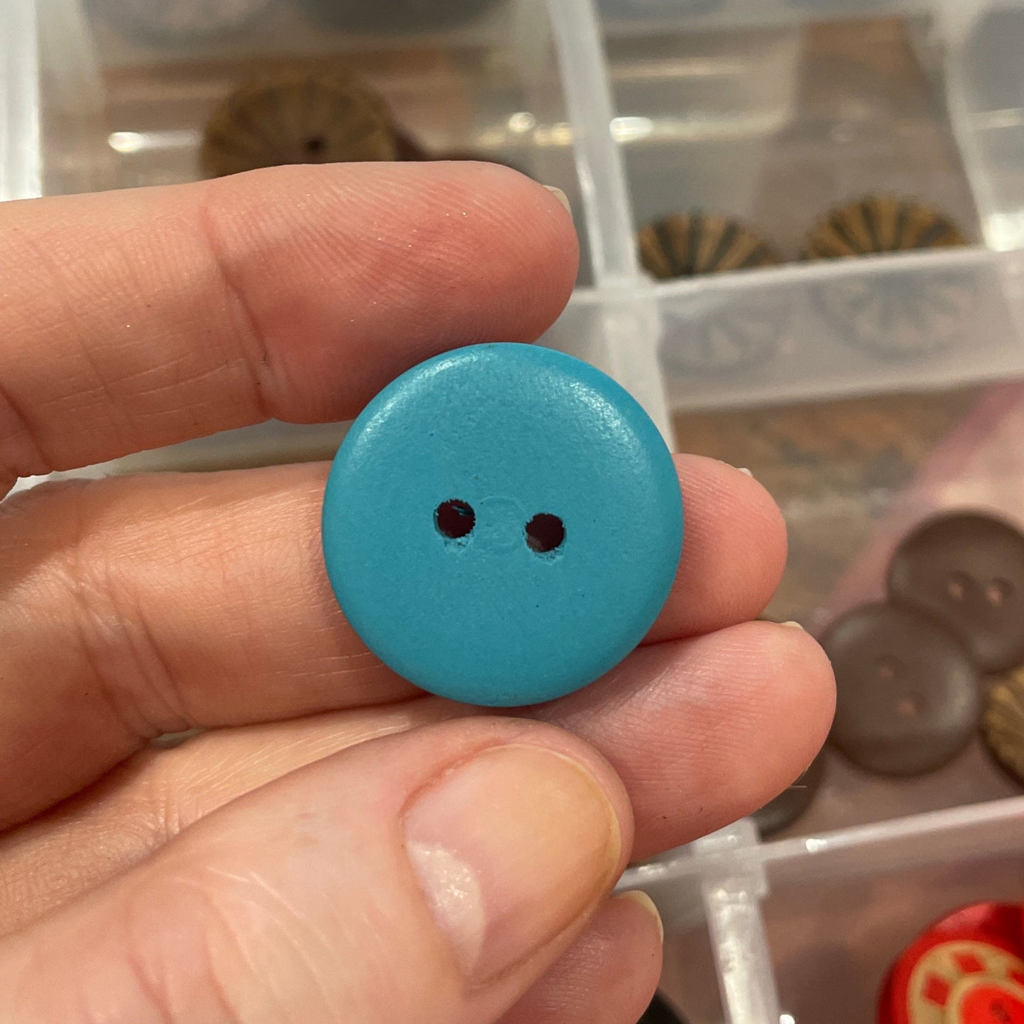 Hand holding a blue button with a container of assorted buttons in the background