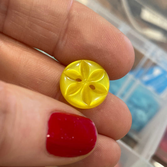 Hand holding a yellow button with a red nail polish, surrounded by more buttons in a container.