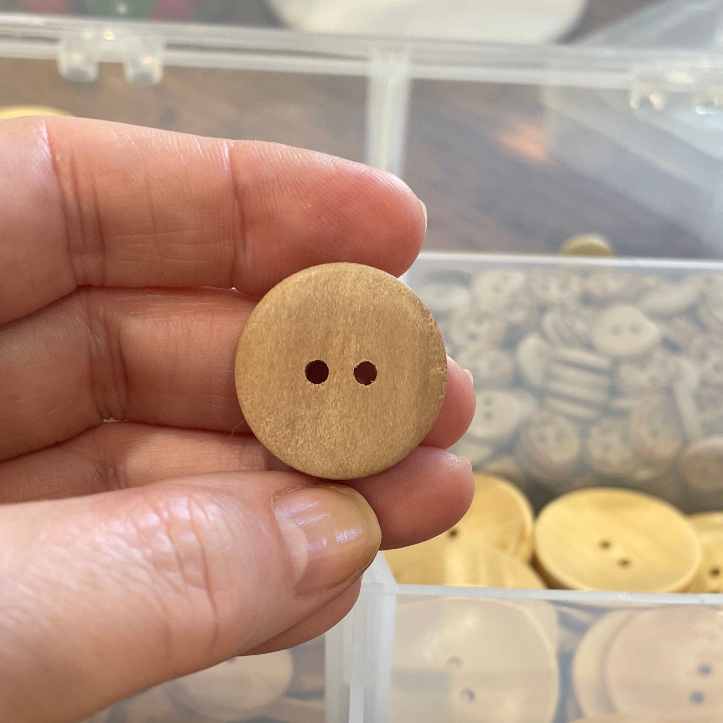 Hand holding a wooden button with a display of various buttons in the background
