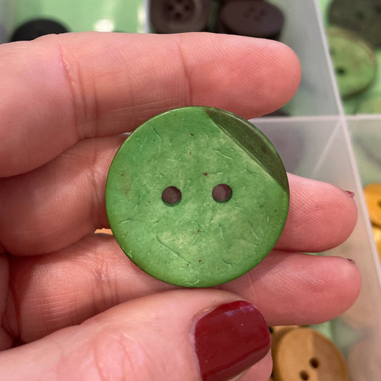 Hand holding a green button with a collection of buttons in the background